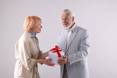 Açık gri arka planda hediye kutusu olan sevimli yaşlı çift.