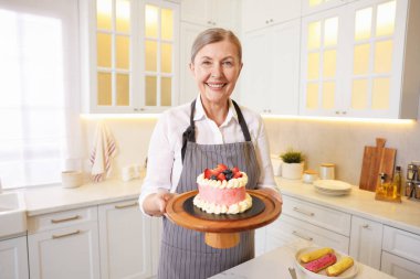 Gülümseyen pasta şefi elinde pastayla mutfakta bekliyor.