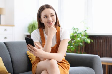 Evdeki kanepede akıllı telefon kullanan genç bir kız.