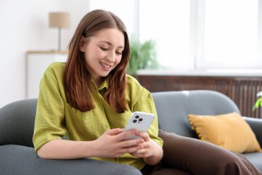 Evdeki kanepede akıllı telefon kullanan genç bir kız.