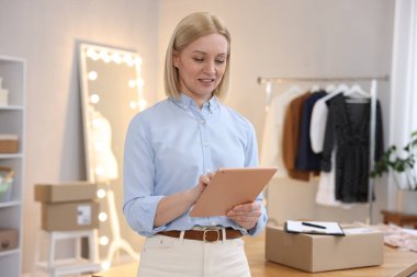 Dükkan sahibi, terzi dükkanında paketle birlikte masanın yanında tablet kullanıyor.