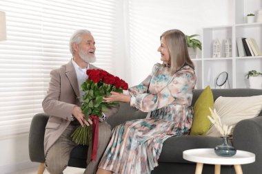 Evdeki kanepede mutlu karısına gül buketi sunan bir adam.