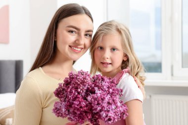 Anne ve kızı evde bir buket leylak çiçekleriyle