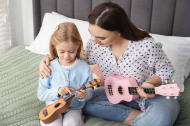 Küçük bir kıza evde gitar çalmayı öğreten genç bir kadın.