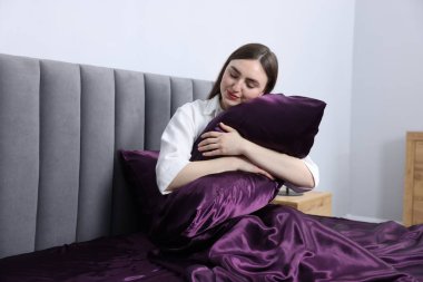 Mor ipek çarşaflarla yatakta yastığa sarılan bir kadın.