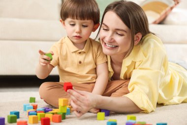 Anne ve oğlu evde renkli küplerle oynuyorlar.