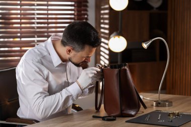 Kapalı mekânda deri çanta değerlendirmesi yapan bir eksper.