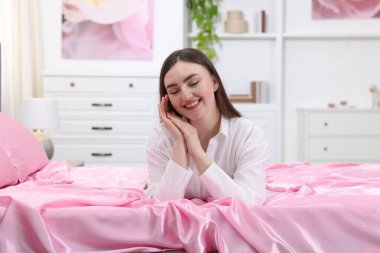 Yatakta pembe ipek çarşaflarla gülümseyen kadın.