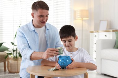 Baba ve oğul evdeki domuz kumbarasına cep harçlığı koyuyor.