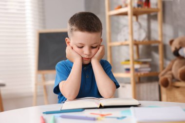 Disleksi. İçerideki masada kitap okuyan küçük çocuk.