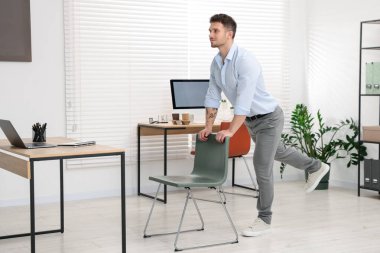 Ofiste sandalyeyle egzersiz yapan yakışıklı adam.