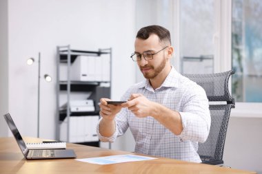 Ofisteki masada akıllı telefondaki tarama uygulamasını kullanarak belgenin fotoğrafını çeken bir adam.