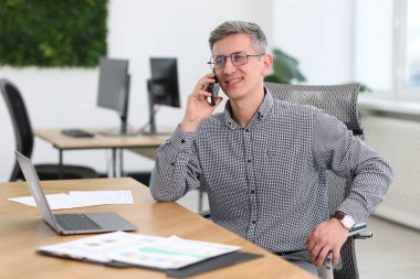 Ofiste akıllı telefondan konuşan gülümseyen iş adamı.