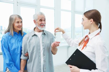 Elinde not panosuyla gülümseyen bir emlakçı evdeki yeni sahibine evin anahtarını veriyor.