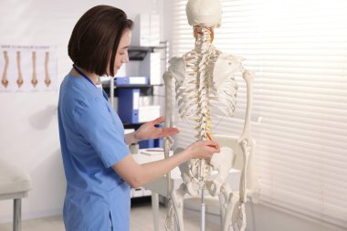 Doktor klinikteki insan iskeleti parçalarına işaret ediyor.