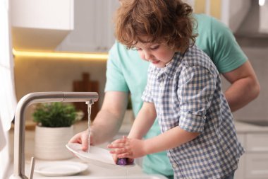 Baba ve oğlu evde birlikte bulaşık yıkıyorlar.