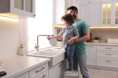 Baba ve oğlu evde birlikte bulaşık yıkıyorlar.
