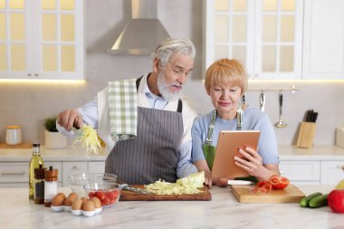 Büyük çift mutfakta birlikte yemek pişirirken tablet kullanıyor.