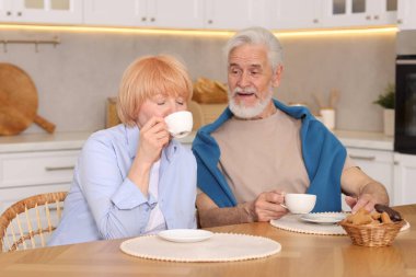Mutfaktaki ahşap masada birlikte kahvaltı eden sevimli yaşlı çift.