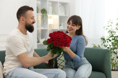 Evdeki kanepede sevgili karısına bir buket kırmızı gül sunan bir adam.