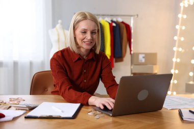 İşyeri sahibi, terzi dükkanındaki masada dizüstü bilgisayarla çalışıyor.