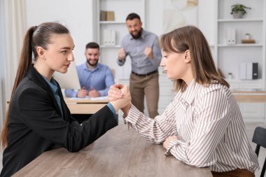 İş kadınları ofiste tahta masada bilek güreşi yapıyor, seçici bir odak noktası var.