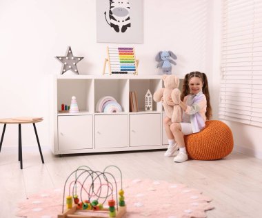 Küçük kız oyun odasında oyuncak ayıyla oynuyor.