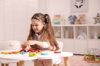 Motor beceri geliştirme. Beyaz masada renkli ahşap parçalarla oynayan küçük bir kız.