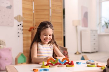 Motor beceri geliştirme. İçerideki masada renkli ahşap parçalarla oynayan küçük kız.