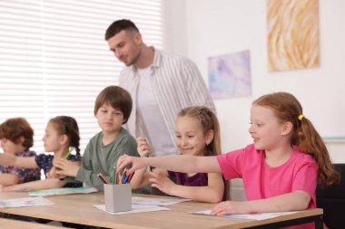 Çocuklara resim yapmayı öğreten adam kapalı alanda resim dersi veriyor, seçici bir odak.