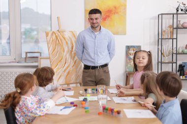 Çocuklara resim dersinde resim yapmayı öğreten bir adam.