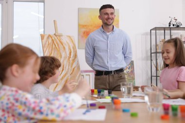 Çocuklara resim dersinde resim yapmayı öğreten bir adam.