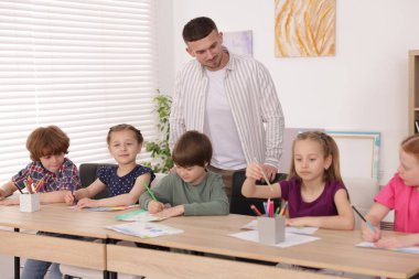 Çocuklara resim dersinde resim yapmayı öğreten bir adam.