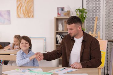 Çocuğa resim çizmeyi öğreten adam kapalı alanda resim dersi veriyor, seçici odaklanıyor.