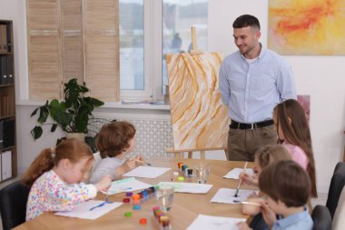 Çocuklara resim dersinde resim yapmayı öğreten bir adam.