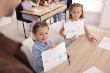 Çocuklar resim dersinde öğretmenlerine resimlerini gösteriyorlar, seçici bir şekilde.