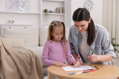 Anne kızına evde, masada resim yapmayı öğretiyor.