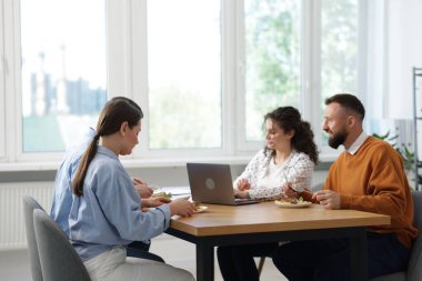 İş arkadaşları ofiste yemek yiyor ve sohbet ediyorlar.