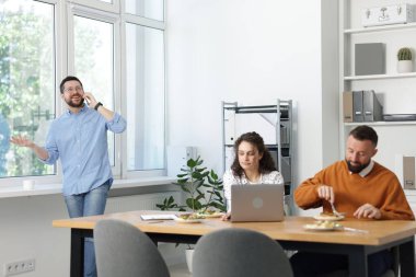 İş arkadaşları ofiste yemek yiyor ve sohbet ediyorlar.