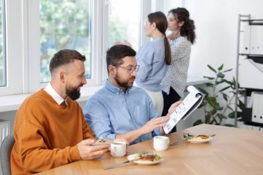 İş arkadaşları yemek yiyor ve ofiste öğle arasında iş tartışıyorlar.