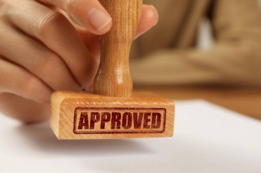 Onaylandı. Masada boş kağıt damgalayan kadın, yakın plan.