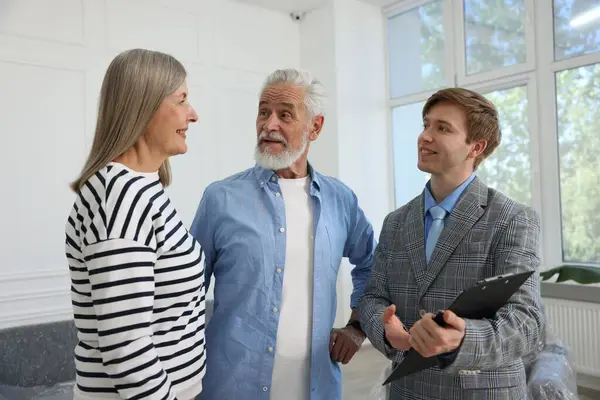 Gülümseyen bir emlakçı pano ile evde çiftlerle çalışıyor.