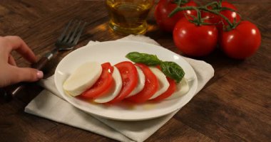 Ahşap masada domatesli ve fesleğenli mozzarella yiyen kadın, yakın plan.