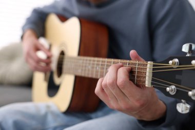 Genç adam kanepede gitar çalıyor, yakın plan.