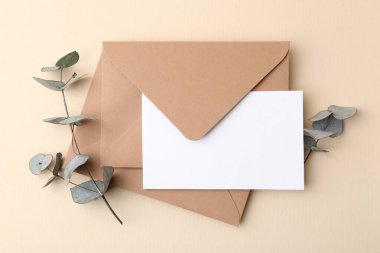 Boş tebrik kartı, zarflar ve okaliptüs yaprakları bej arka planda, düz uzanmış