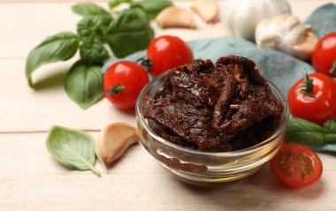 Lezzetli güneşte kurutulmuş domatesler, taze sebzeler, fesleğen ve sarımsak beyaz ahşap masada, yakın plan.