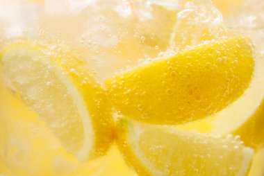 Sarı arka planda limon dilimleri ve buzla soda tazeleniyor. Yakın plan.