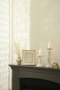 Beyaz duvarın yanındaki şöminede yanan mumlar ve diğer dekorlarla süslü şamdanlar.