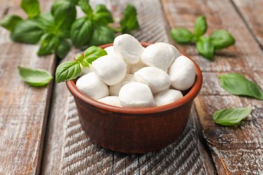 Lezzetli mozzarella peynir topları kasede ve fesleğen ahşap masada, yakın plan.