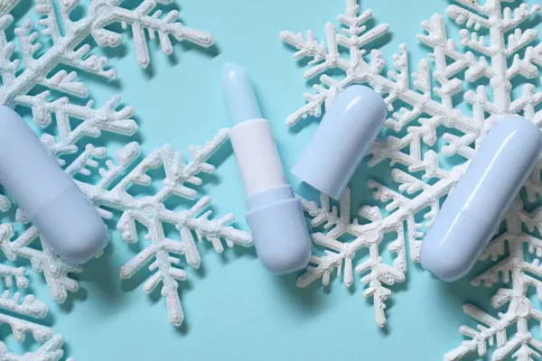 Nemlendirici dudak kremi ve açık mavi arka planda Noel dekoru, düz yatış. Kış bakımı